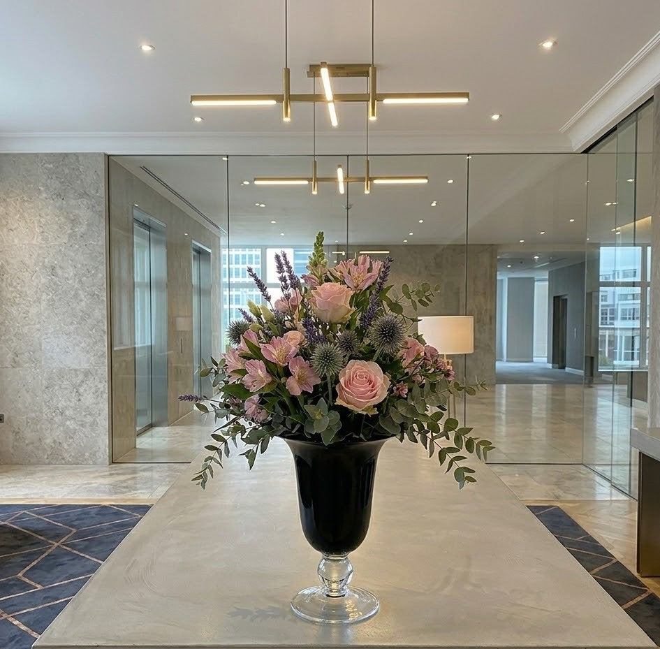 Modern zakelijk bloemstuk in een glazen vaas op een witte kantoorreceptie door Business Plants.